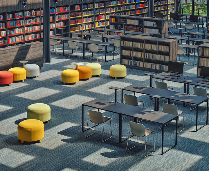 A modern coworking space furnished with office furniture, bookcases and colourful poufs.