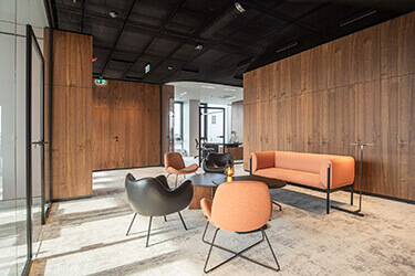 Elegant meeting space with orange sofa, black armchairs and wooden wall panels.