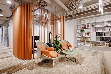 Lounge area in the office with orange armchairs, round table and openwork partition of vertical lamellas.