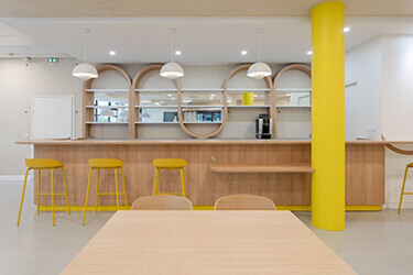 Minimalist dining area with wooden bar, yellow bar stools and decorative arches in the wall surround.