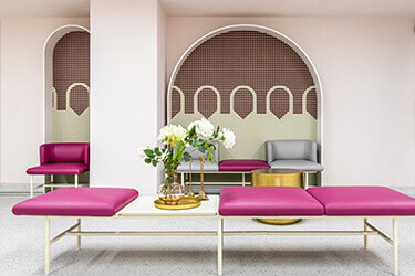 Modern waiting room with pink modular seating, decorative arches on the walls and auxiliary tables.
