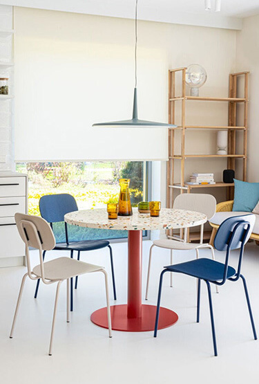 Bright interior of a home kitchen with colourful chairs and a round table with a red leg.