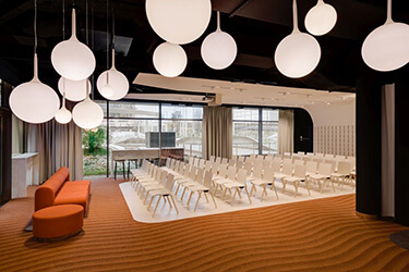 Event room with rows of white chairs, spherical ceiling lighting and orange sofa.