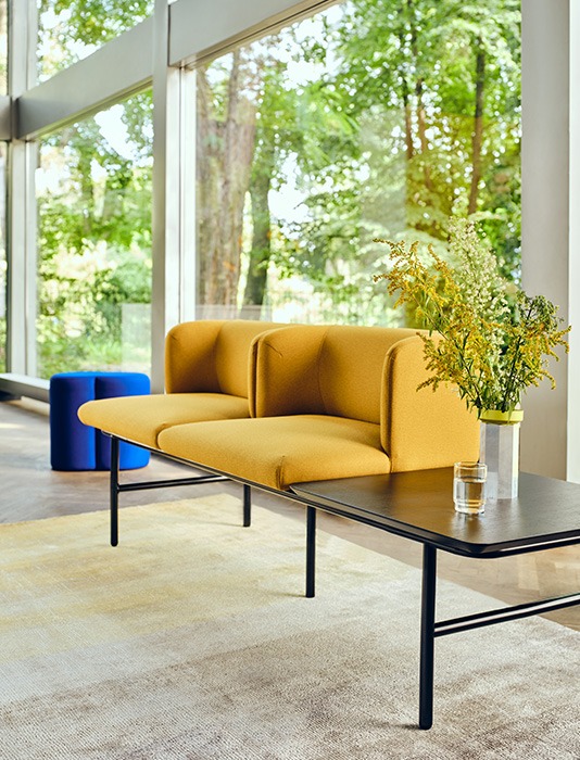 Modern Stilt sofa in light beige colour, in a space with large windows and a table