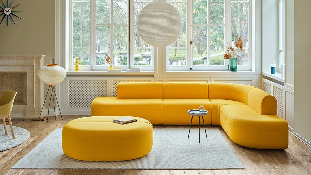 Beige Lotus double sofa with cushions, in a living room with light curtains and wooden floor