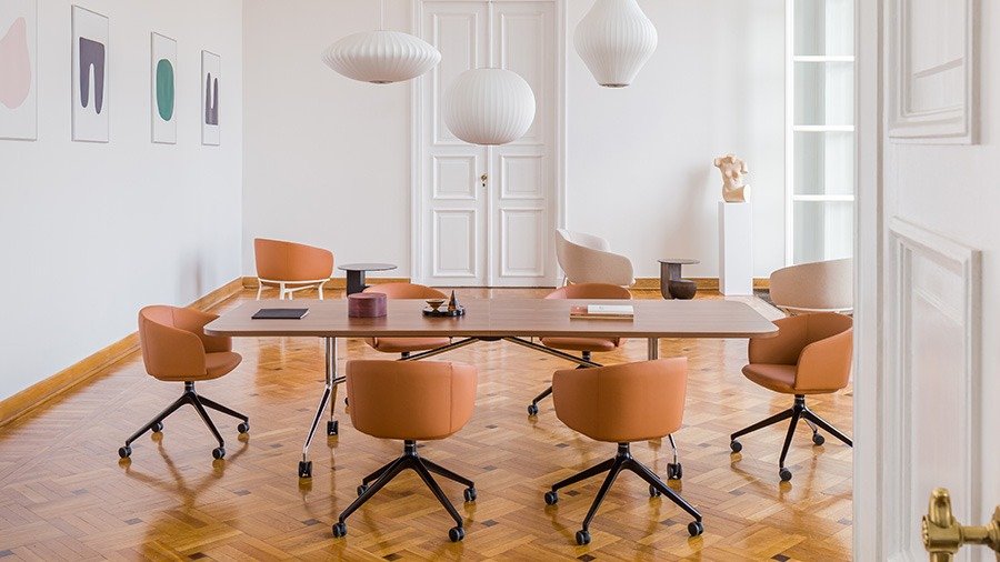 Conference room with a large wooden table and six brown chairs on castors.