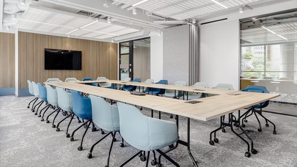 Modern conference room with a long light-coloured table and a row of blue chairs on castors.
