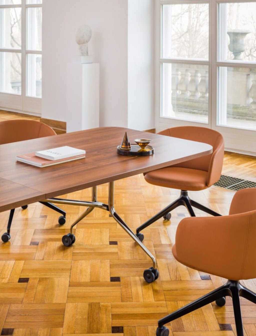 Close-up of a wooden conference table with brown chairs on castors by the window.
