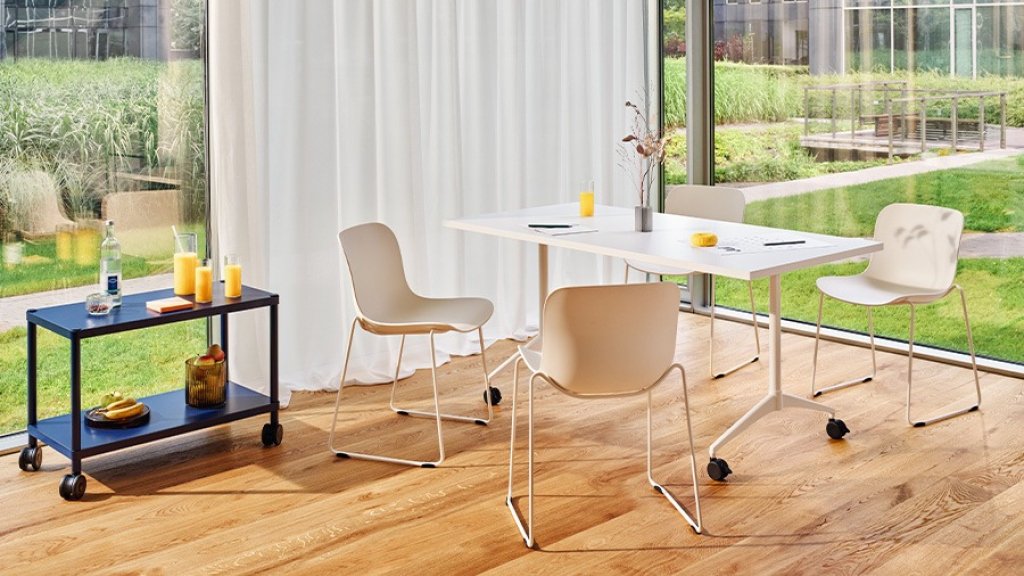 Meeting room with a white table on castors and four light-coloured chairs by the window overlooking the garden.