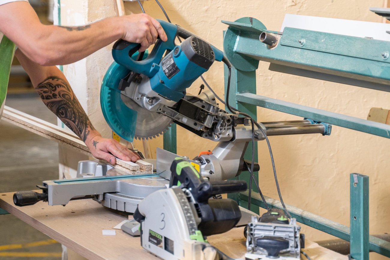 Un employé de la menuiserie découpe un panneau de meuble sur mesure pour la fabrication de meubles atypiques.