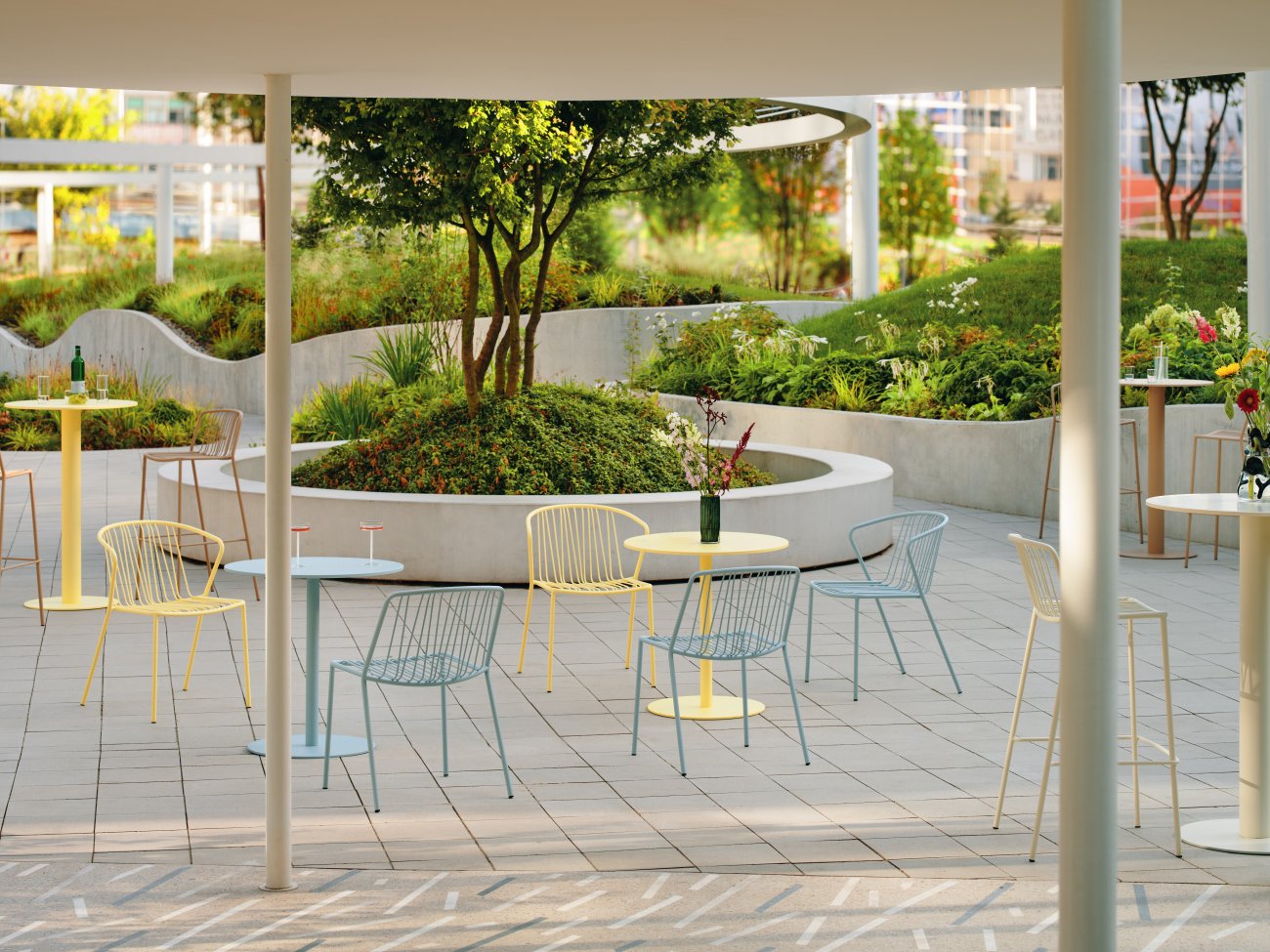 Espace terrasse moderne avec chaises et tables métalliques aux couleurs pastel, entouré de verdure