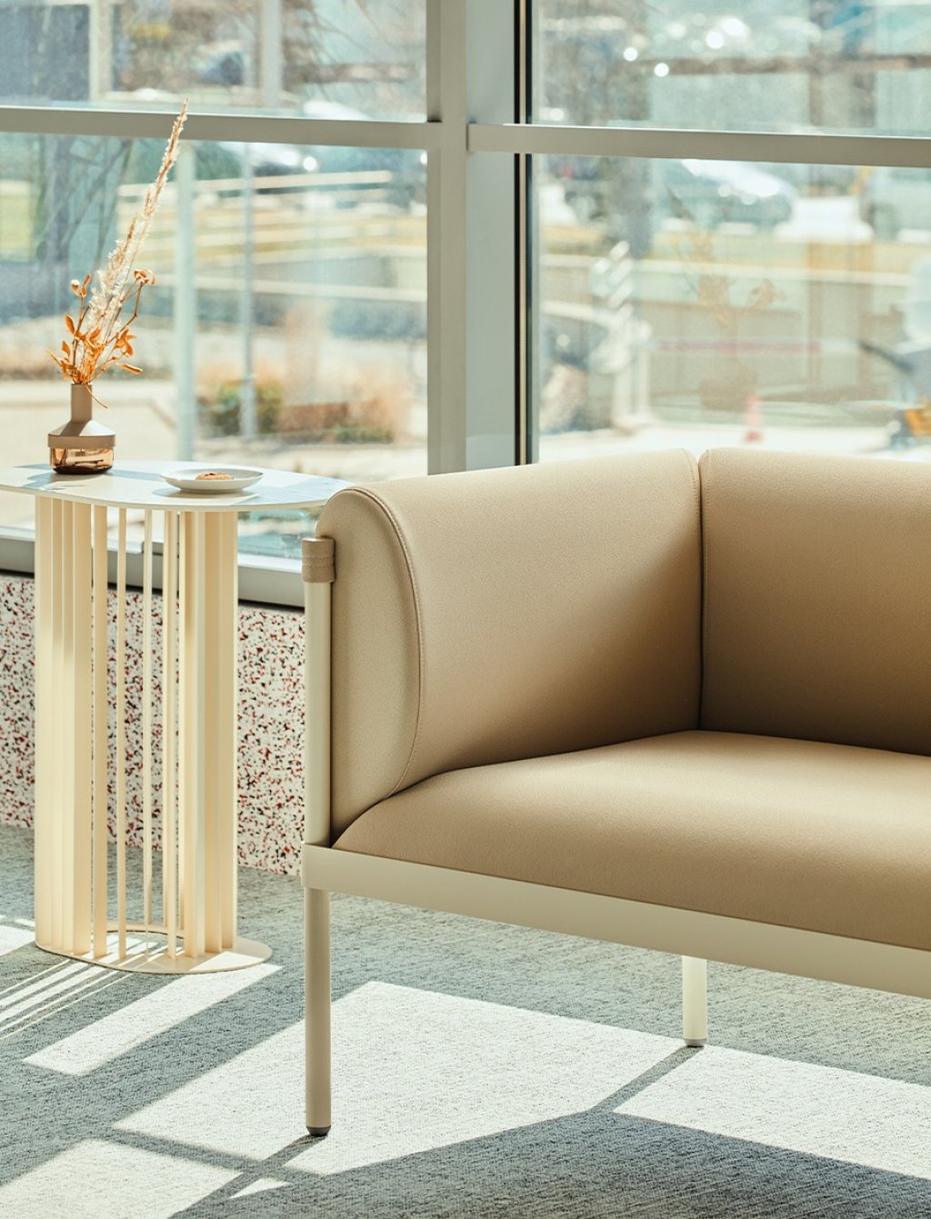 Modern Stilt sofa in light beige colour, in a space with large windows and a table