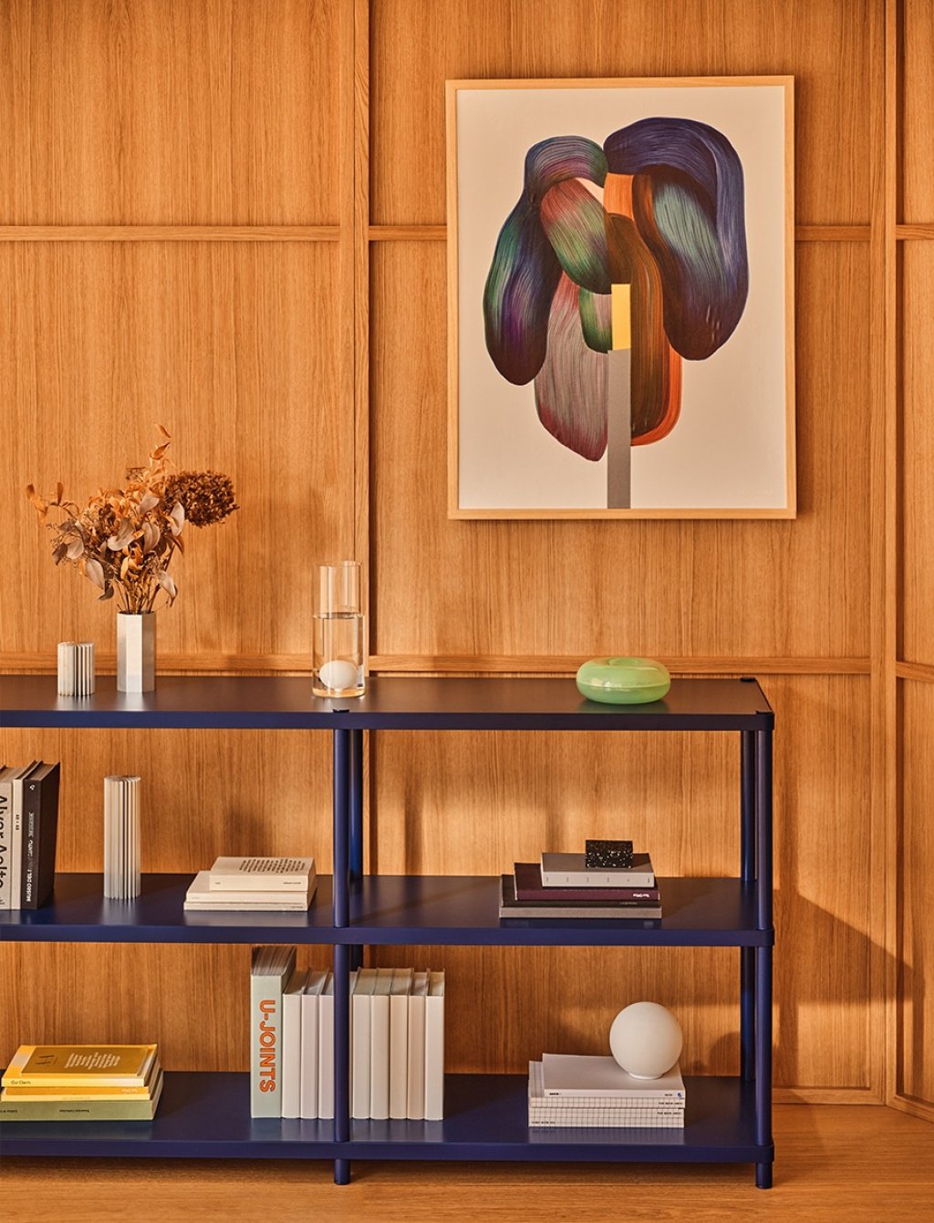 Navy blue shelving unit with books against a wood wall, with framed artwork and decor