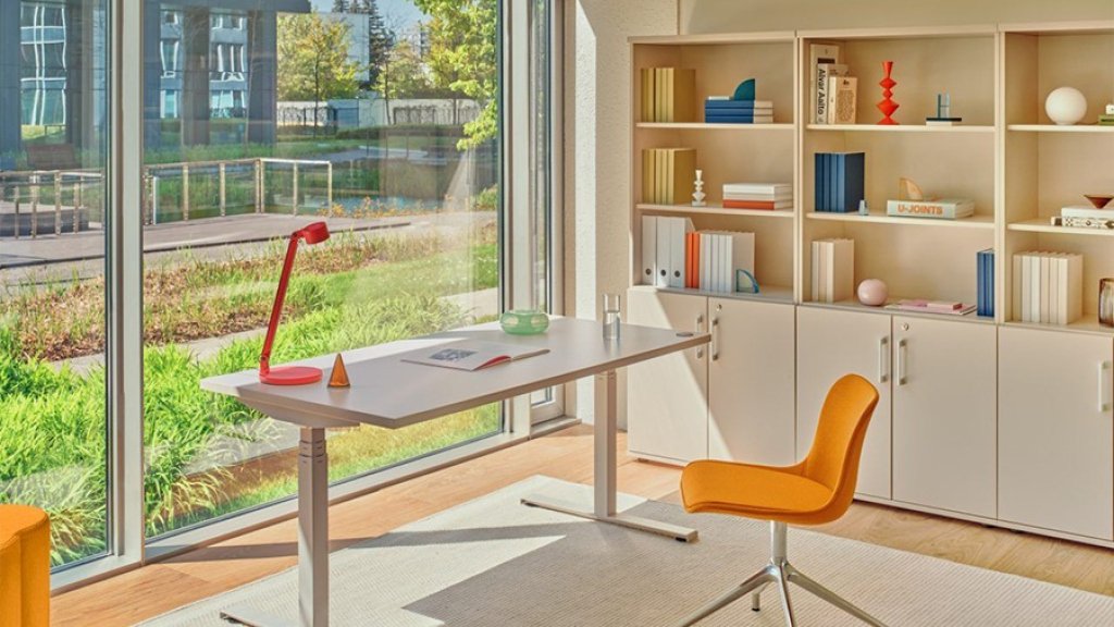 Bright home office by large windows: white desk, orange chair and bookcase with books