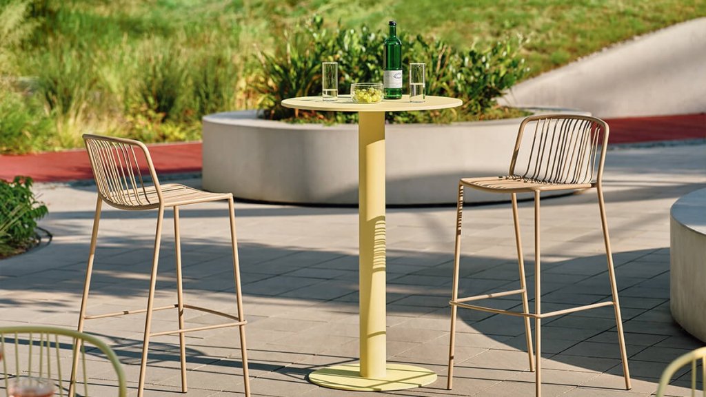 Gartenbarhocker Bris aus Metall mit schmalen Rückenlehnen an einem runden gelben Tisch.