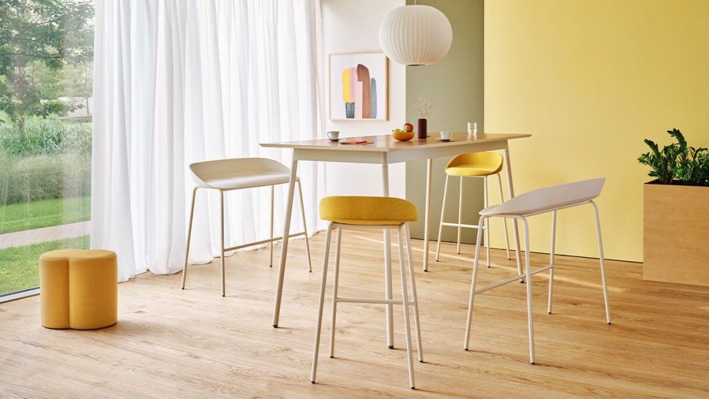 Bunte gepolsterte Barhocker ohne Rückenlehne an einem rechteckigen Tisch in einem pastellfarbenen Innenraum.