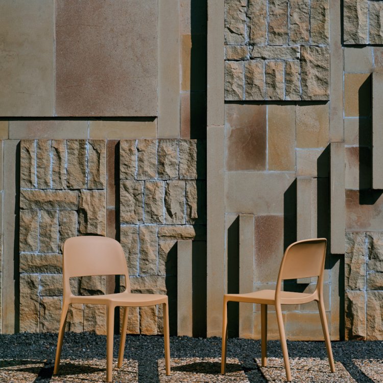 Two brown plastic chairs outside, a sculptural stone wall behind them