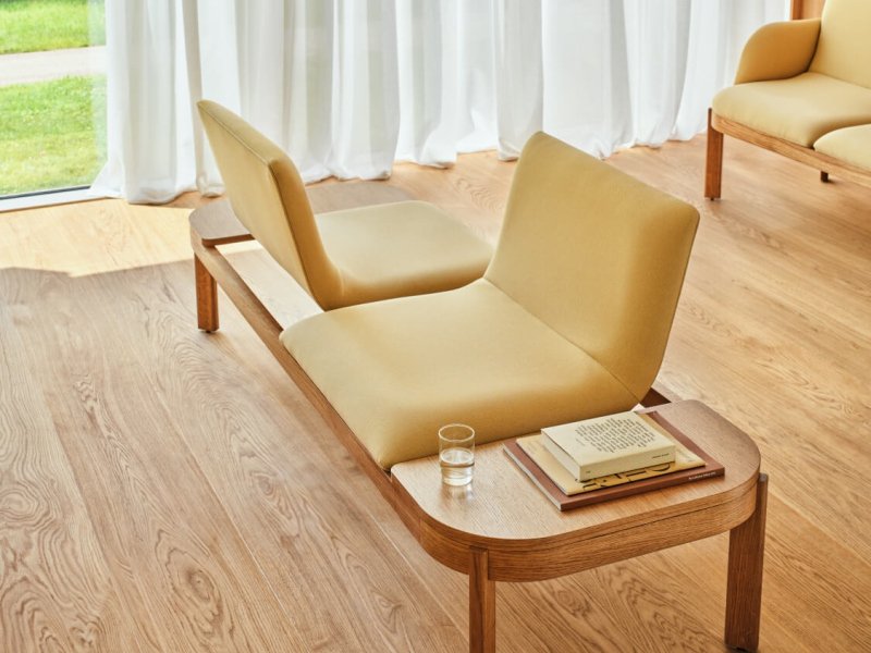Leuchtend gelbes Sofa auf einem Holzsockel mit entgegengesetzten Sitzrichtungen