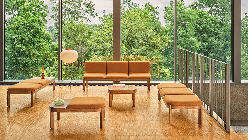 A set of upholstered modular seating and wooden tables in a space overlooking greenery