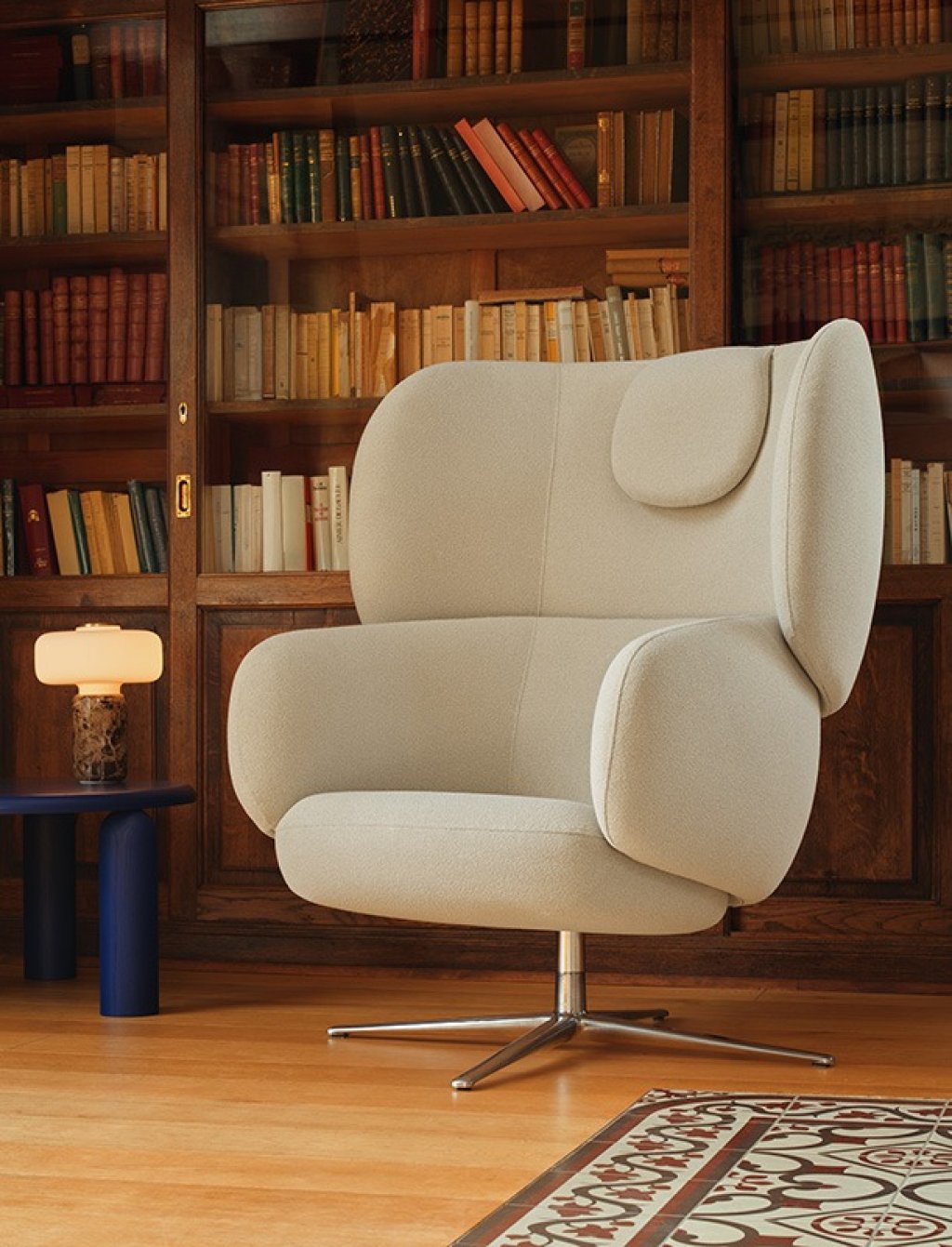Upholstered lounge chair with a high backrest and swivel base, set against a bookcase